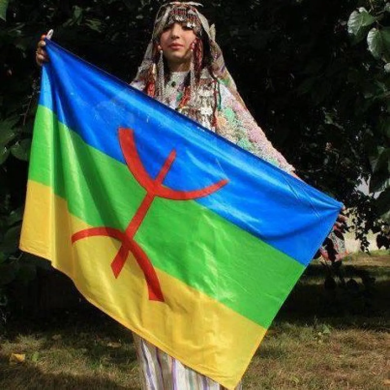 An Amazigh woman in traditional costume with the Amazigh flag
