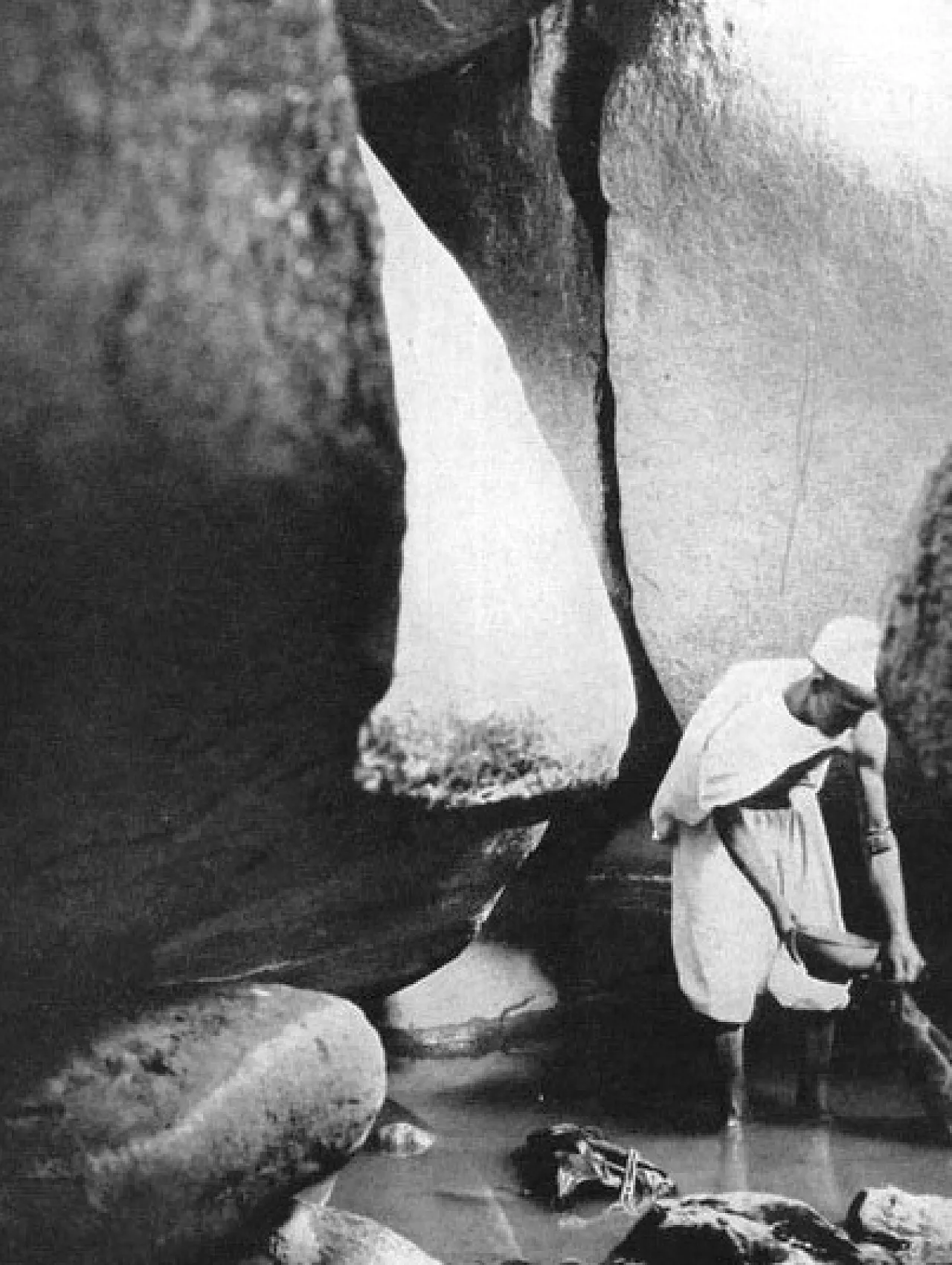 Figure 2:  One of Hassanein’s helpers filling water in a goatskin from one of Awaynat springs (1923). These springs, though they may have less water now due to hyper-aridity, but they are still very essential for travelers crossing borders between Libya and Sudan.  (Photo: after Saharasafaris.org)