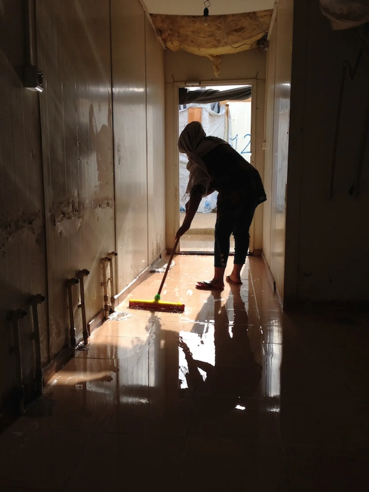 A young woman clears flood waters from a communal area (Photo: Tom Westcott)