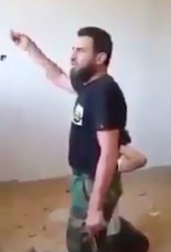 The gunman speaking while his victim kneels behind him (Social media screen grab)